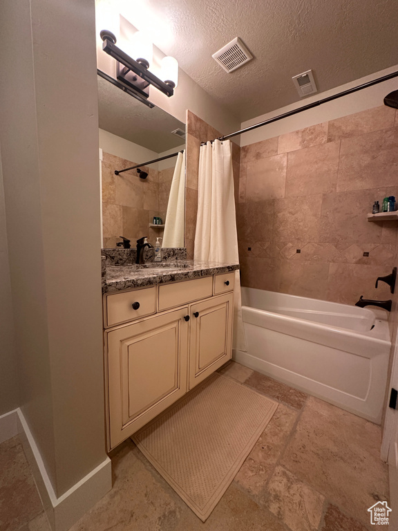Full bath with shower / bath combo, vanity, and a textured ceiling