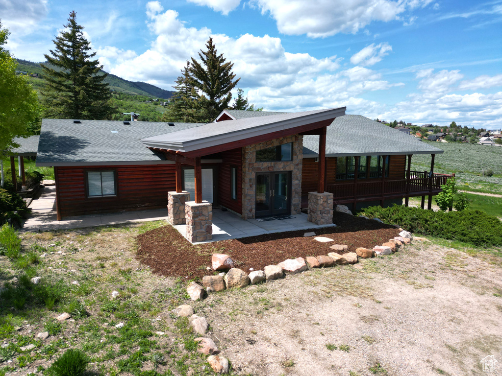Rear view of property featuring a patio, a shingled roof, log veneer siding, and stone siding