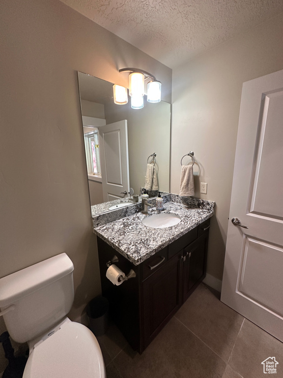 Half bathroom with a textured ceiling, vanity, tile patterned floors, and toilet