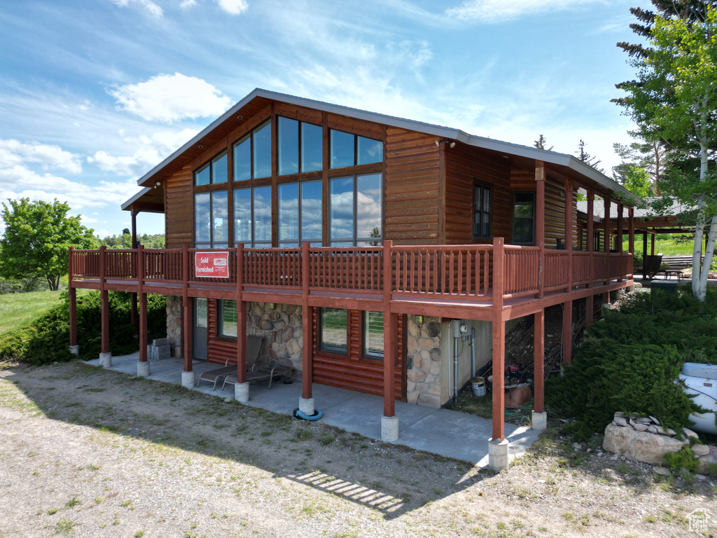 Rear view of property with stone siding, a patio, a deck, and log veneer siding
