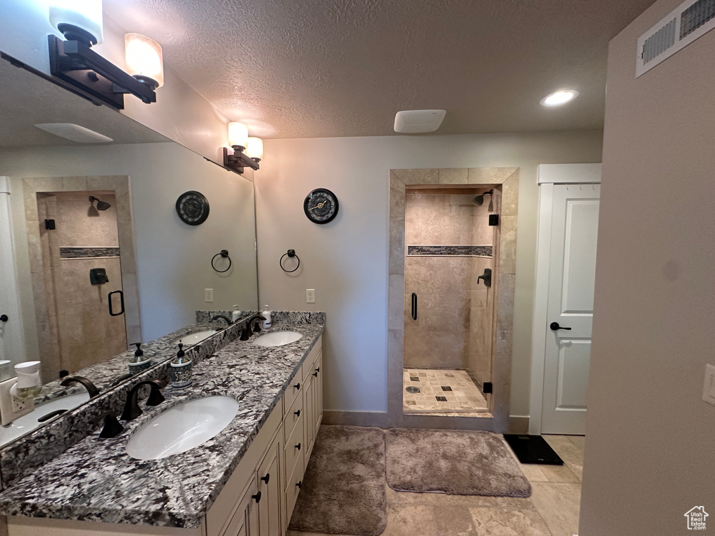 Bathroom featuring double vanity, a shower stall, baseboards, and a textured ceiling