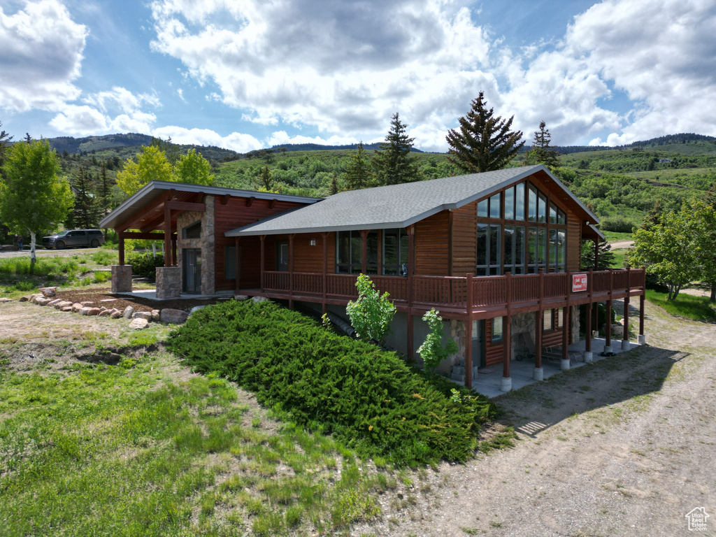 View of front of property with stone siding, a patio area, a deck with mountain view, and faux log siding