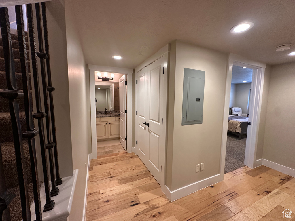 Corridor with electric panel, light wood-type flooring, baseboards, and recessed lighting