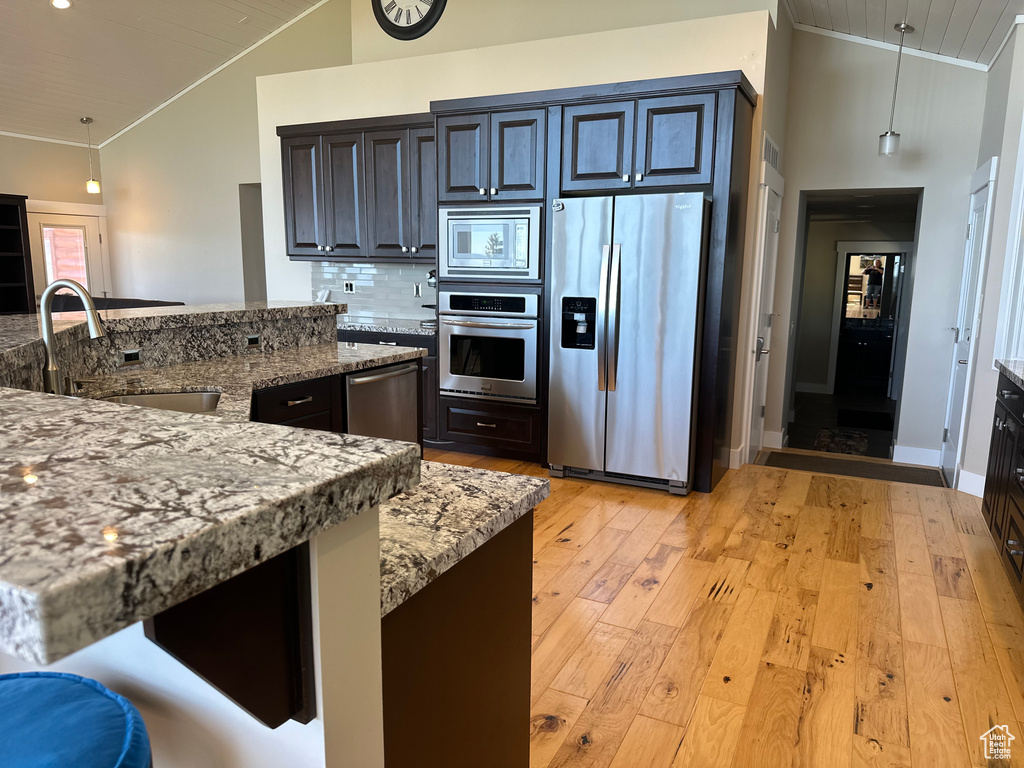 Kitchen with appliances with stainless steel finishes, a sink, crown molding, light wood-type flooring, and light stone counters