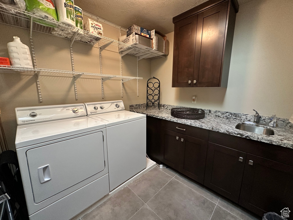Laundry area with washing machine and clothes dryer, light tile patterned floors, a textured ceiling, and cabinet space