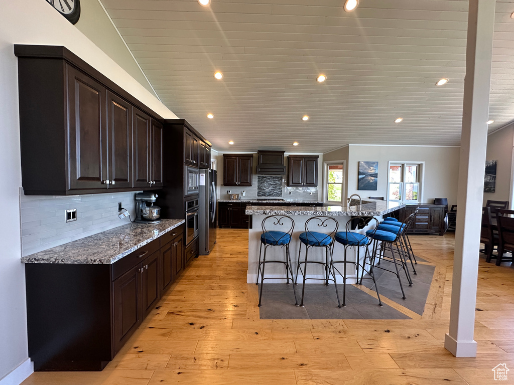 Kitchen featuring a breakfast bar, freestanding refrigerator, a large island with sink, light stone counters, and recessed lighting