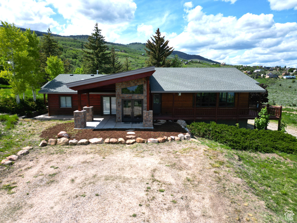 Rear view of house with french doors, roof with shingles, a mountain view, and stone siding