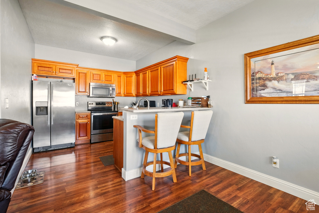 Kitchen with stainless steel appliances, a peninsula, dark wood-type flooring, light countertops, and baseboards