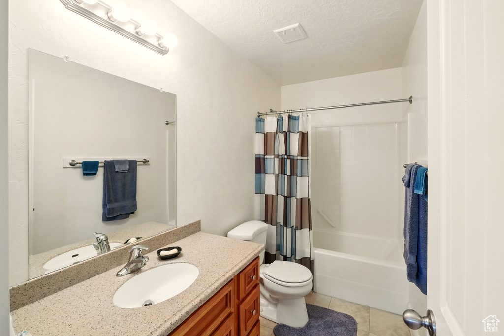 Bathroom with vanity, tile patterned floors, shower / bath combination with curtain, toilet, and a textured ceiling