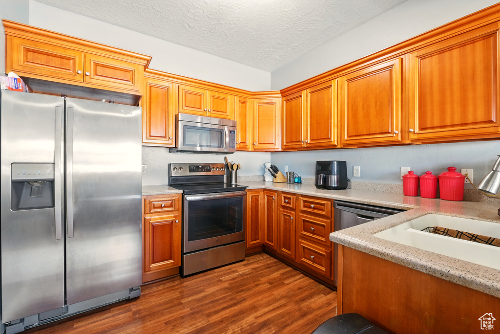 Kitchen with appliances with stainless steel finishes, dark wood finished floors, brown cabinetry, a textured ceiling, and a sink