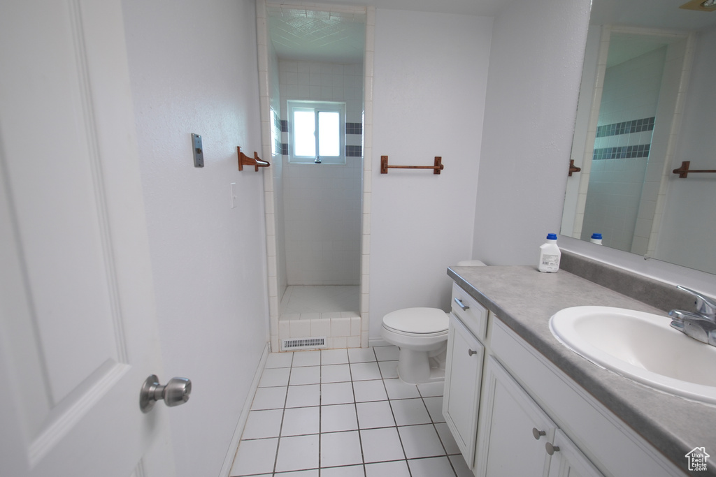 Bathroom featuring vanity, tile patterned flooring, toilet, tiled shower, and baseboards