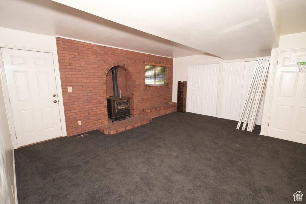 Unfurnished living room with brick wall, a wood stove, and carpet floors