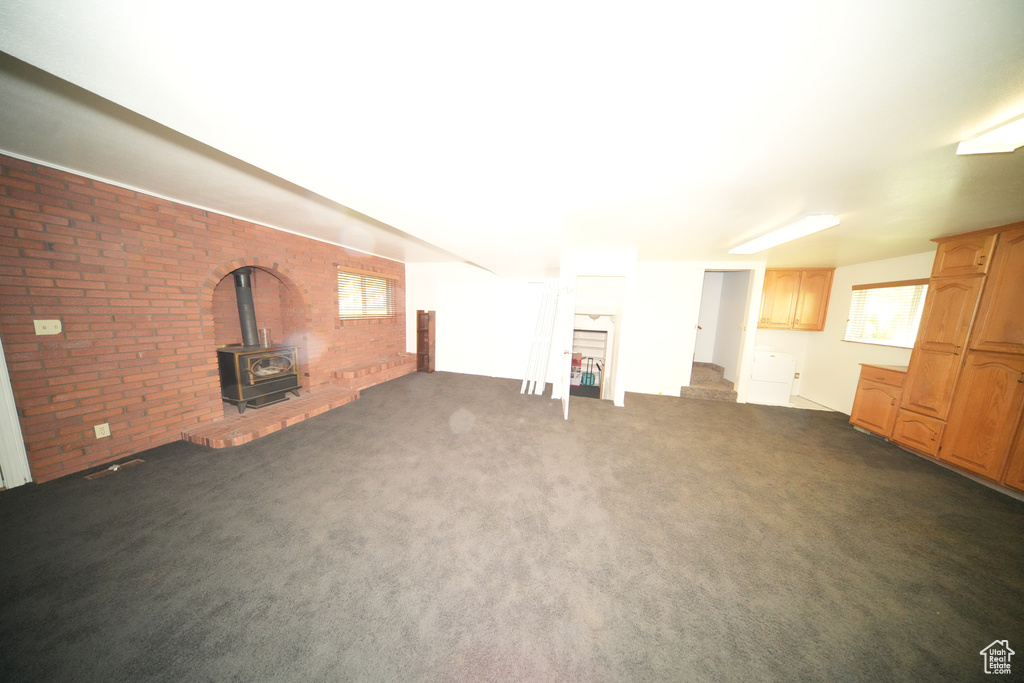 Unfurnished living room featuring brick wall, a wood stove, and dark carpet