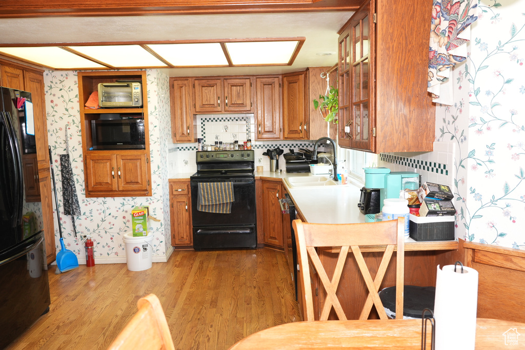 Kitchen with black appliances, a sink, light countertops, brown cabinetry, and wallpapered walls