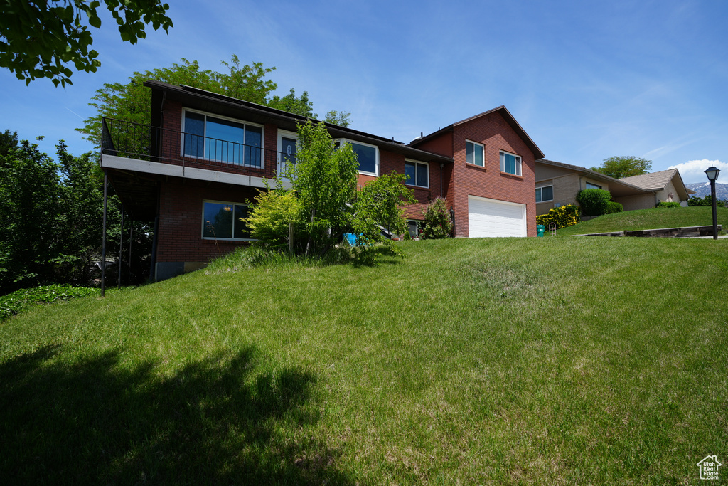 Back of house featuring brick siding, an attached garage, a balcony, and a lawn