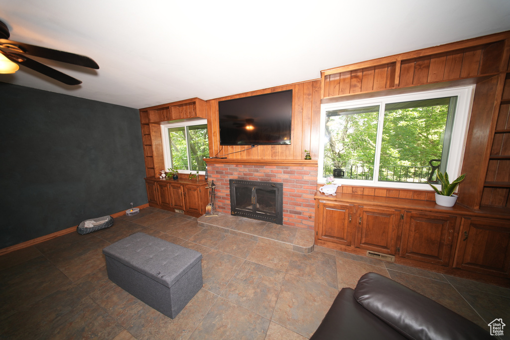 Living room with a ceiling fan, a brick fireplace, wooden walls, and baseboards