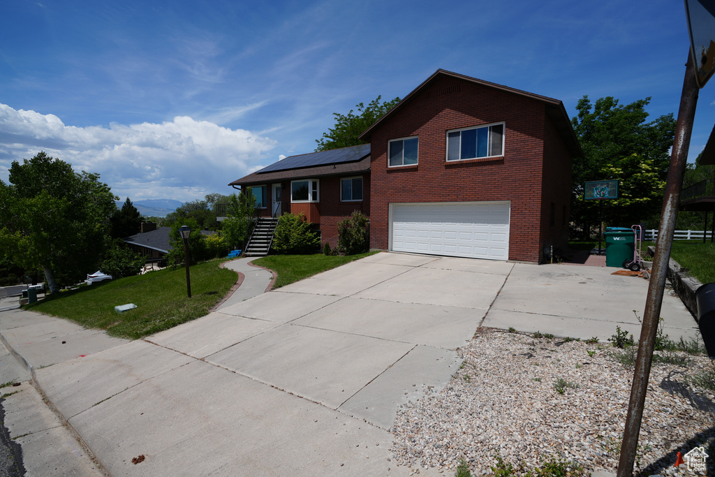 Tri-level home with brick siding, a garage, roof mounted solar panels, driveway, and a front lawn