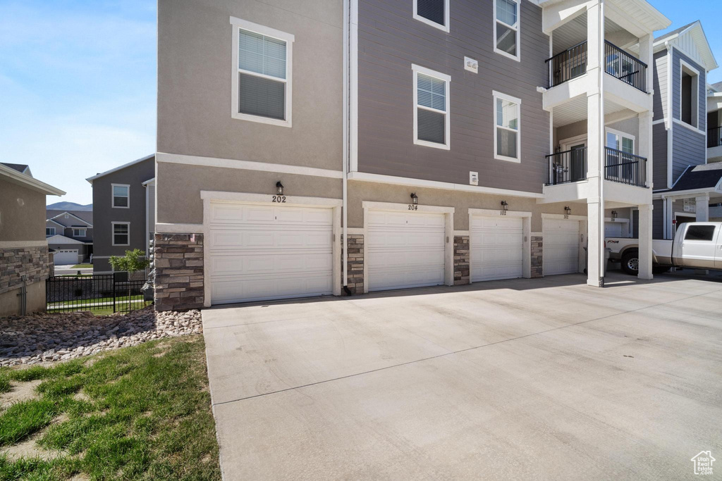 Rear view of property featuring stone siding, driveway, stucco siding, and an attached garage