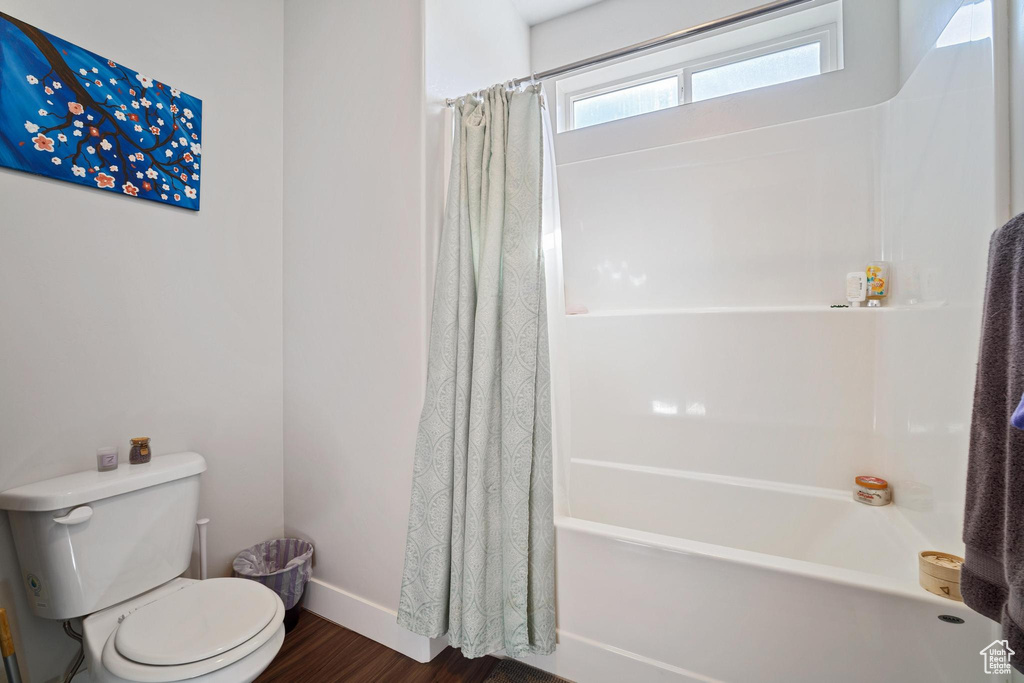 Bathroom featuring wood finished floors, toilet, shower / bath combo with shower curtain, and baseboards