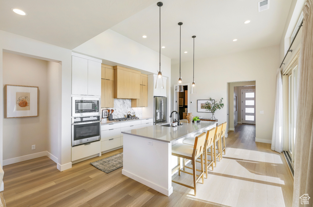 Kitchen with stainless steel appliances, a sink, light wood finished floors, a large island, and a breakfast bar area