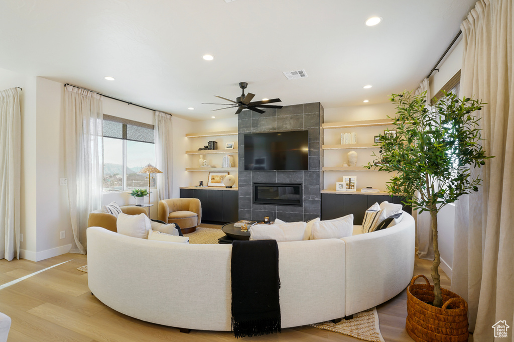 Living area featuring recessed lighting, a tiled fireplace, light wood finished floors, a ceiling fan, and baseboards