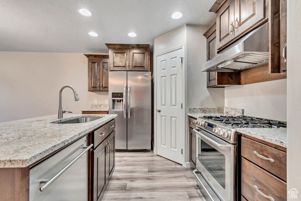 Kitchen featuring stainless steel appliances, a sink, light wood-type flooring, under cabinet range hood, and light stone counters