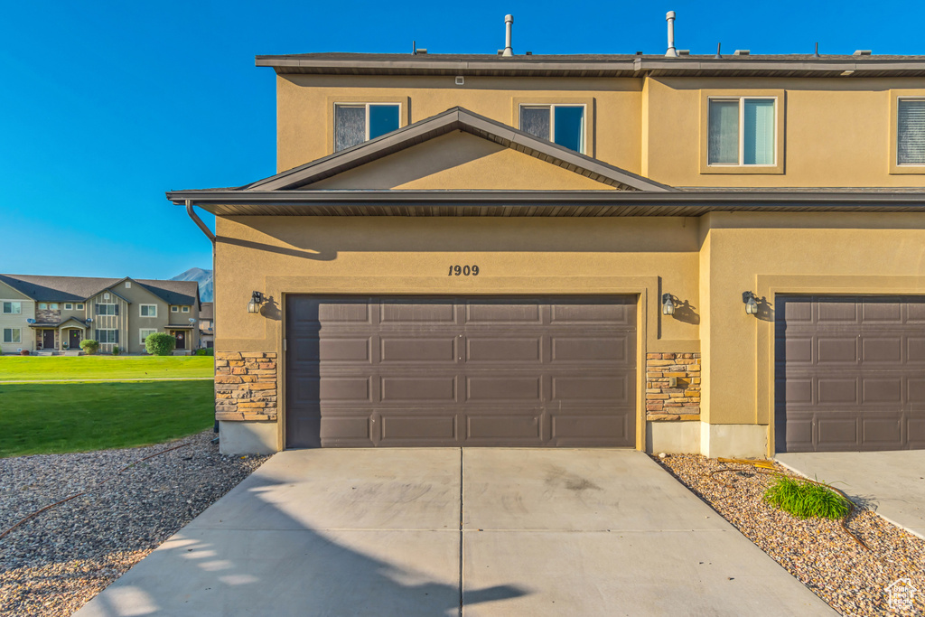 View of front of home with stone siding, driveway, stucco siding, and a garage