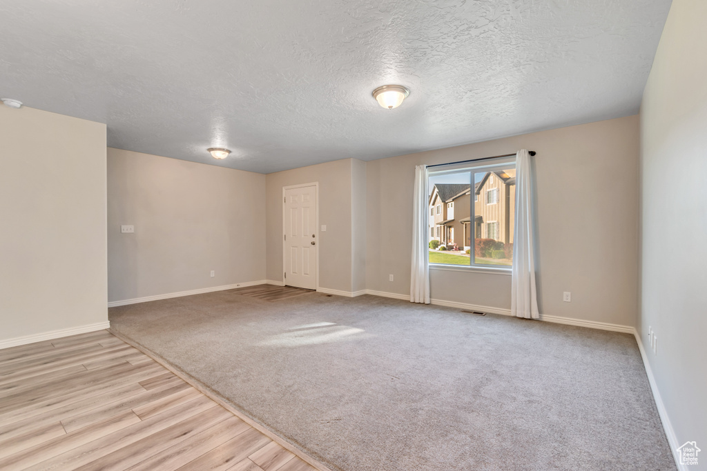 Spare room with wood finished floors, baseboards, a textured ceiling, carpet, and a smoke detector