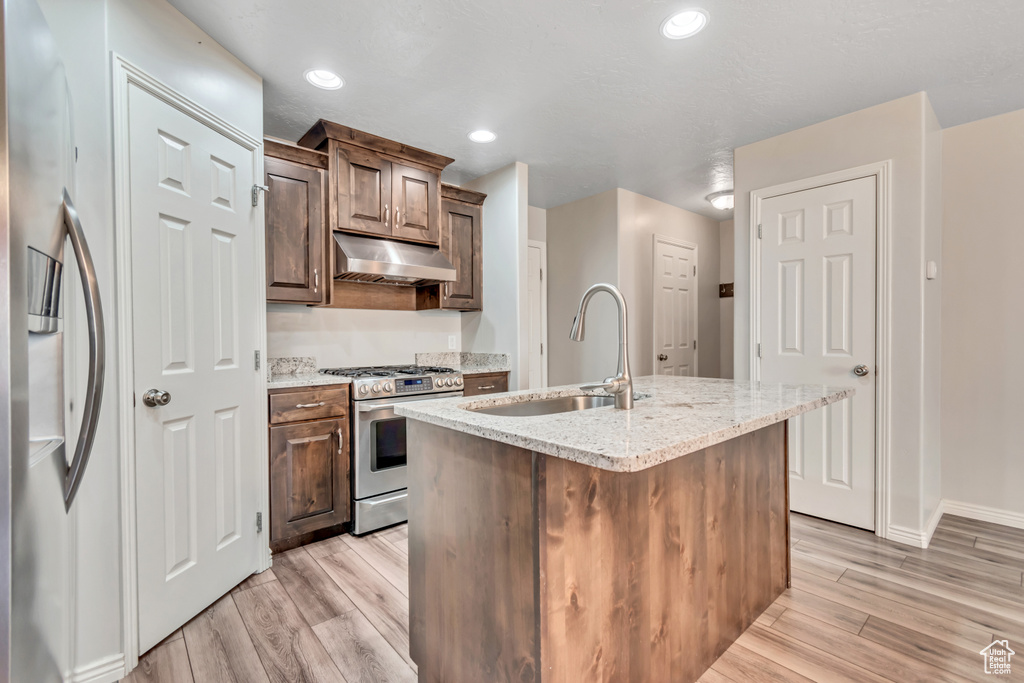 Kitchen with stainless steel appliances, under cabinet range hood, a sink, light wood-style floors, and light stone countertops