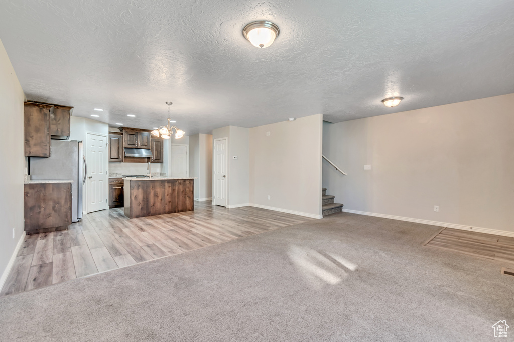 Unfurnished living room featuring baseboards, a chandelier, stairway, light colored carpet, and a textured ceiling