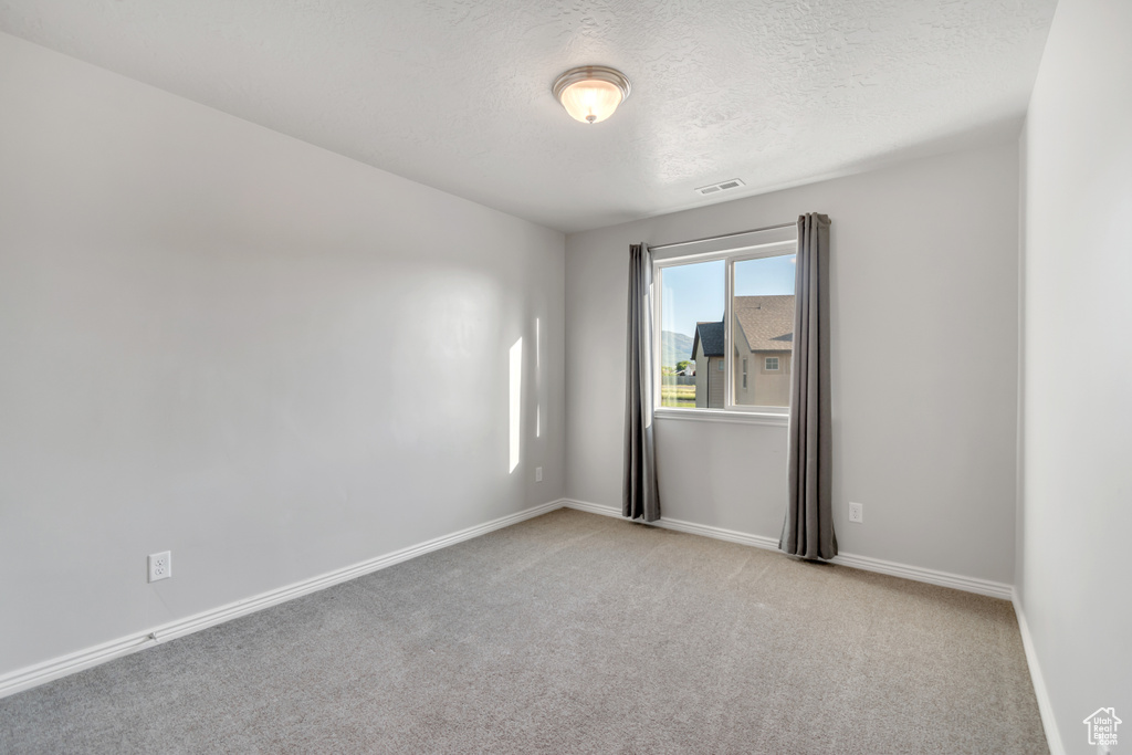 Empty room with a textured ceiling, carpet flooring, and baseboards