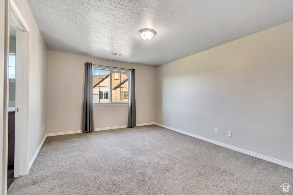 Spare room featuring a textured ceiling, carpet, and baseboards