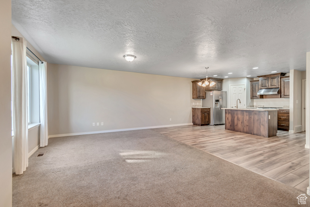 Unfurnished living room featuring baseboards, light carpet, a textured ceiling, a chandelier, and a sink
