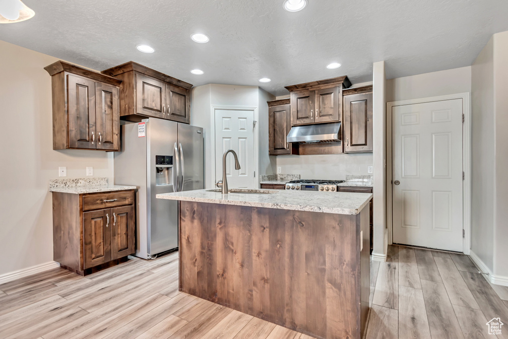 Kitchen with under cabinet range hood, stainless steel fridge with ice dispenser, a sink, light wood finished floors, and recessed lighting