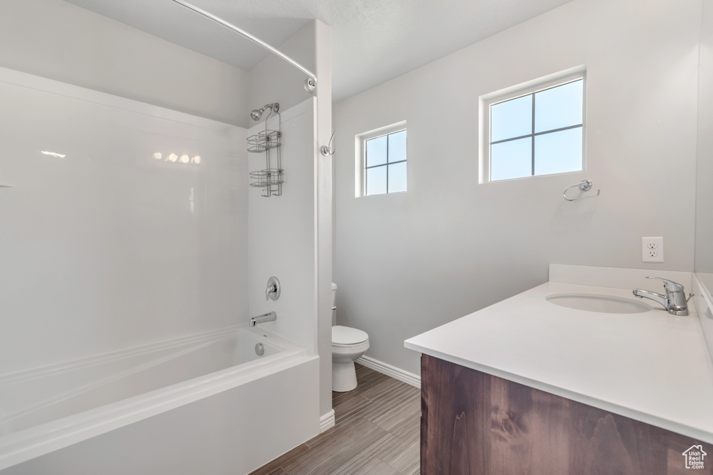 Bathroom featuring shower / tub combination, toilet, vanity, baseboards, and wood finished floors