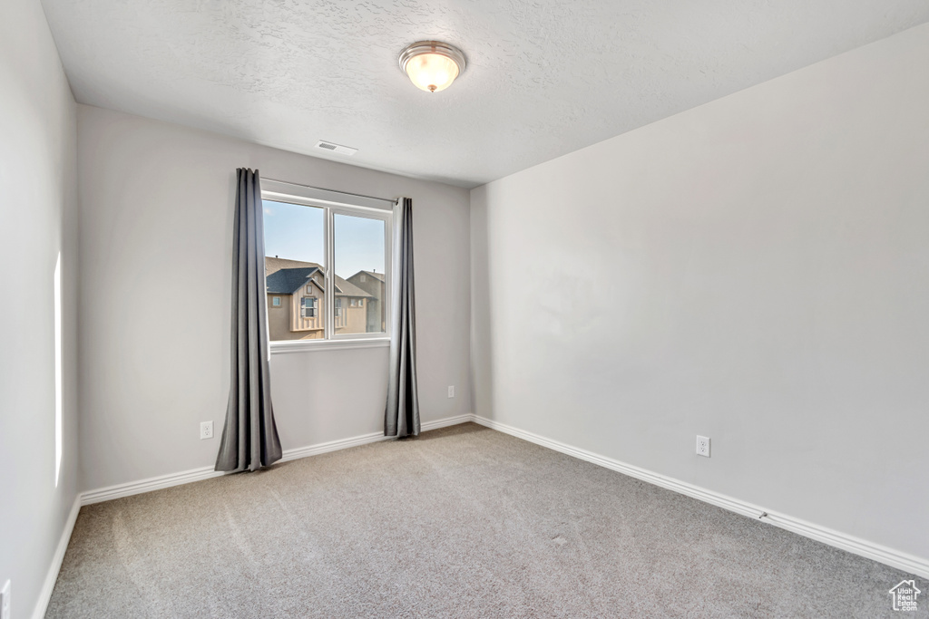 Empty room featuring carpet, a textured ceiling, and baseboards
