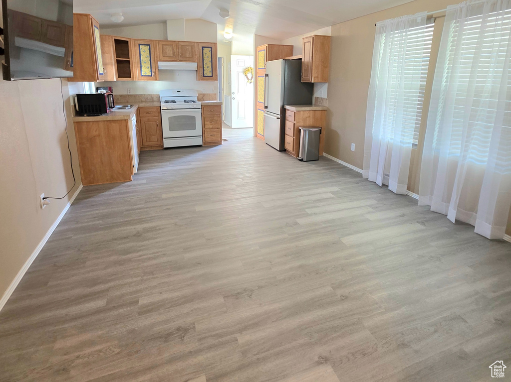 Unfurnished living room featuring vaulted ceiling, baseboards, light wood-style floors, and a sink