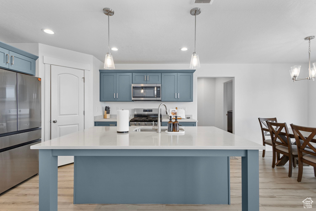 Kitchen featuring appliances with stainless steel finishes, a sink, light countertops, light wood-style flooring, and blue cabinetry
