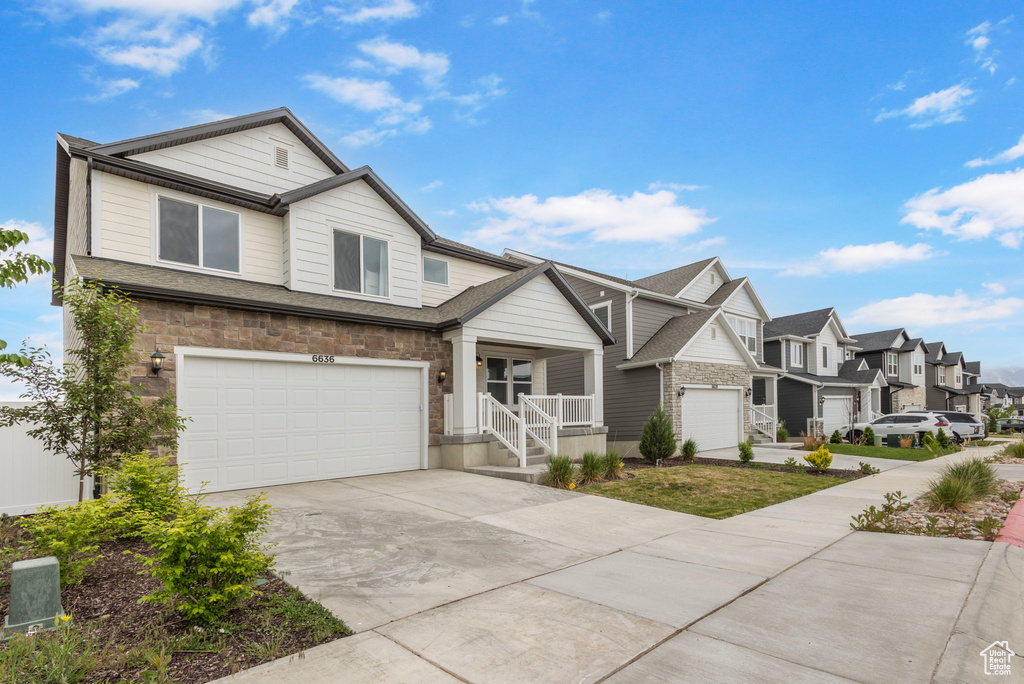 View of front of house with a garage, driveway, a residential view, a porch, and stone siding