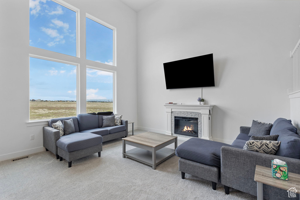 Living area featuring a glass covered fireplace, light colored carpet, baseboards, and a towering ceiling