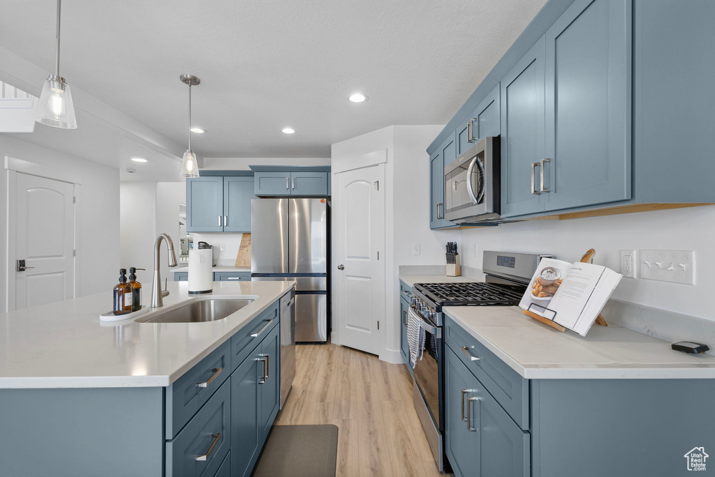 Kitchen with appliances with stainless steel finishes, recessed lighting, a sink, light wood finished floors, and light countertops