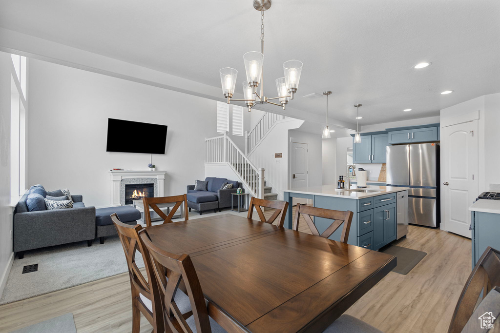 Dining space with light wood finished floors, stairs, recessed lighting, a glass covered fireplace, and a chandelier