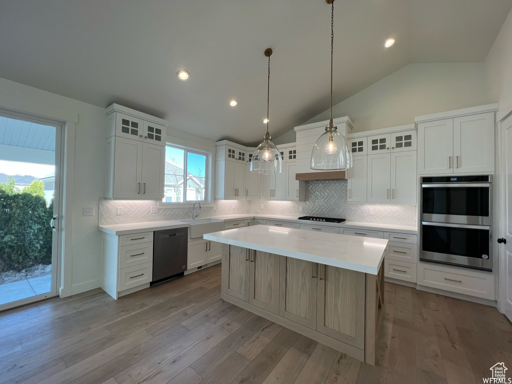 Kitchen featuring appliances with stainless steel finishes, light countertops, a sink, backsplash, and vaulted ceiling