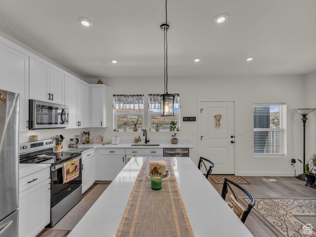 Kitchen with stainless steel appliances, a sink, light countertops, decorative light fixtures, and recessed lighting