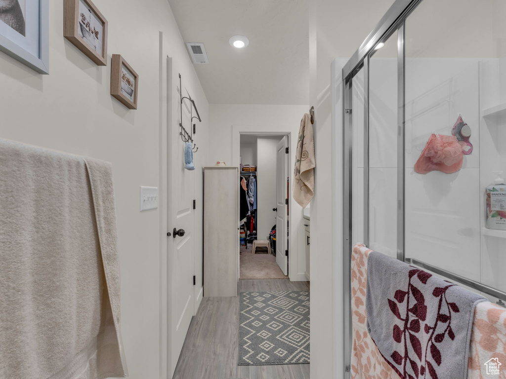 Full bathroom with wood finished floors, a shower stall, a walk in closet, and recessed lighting