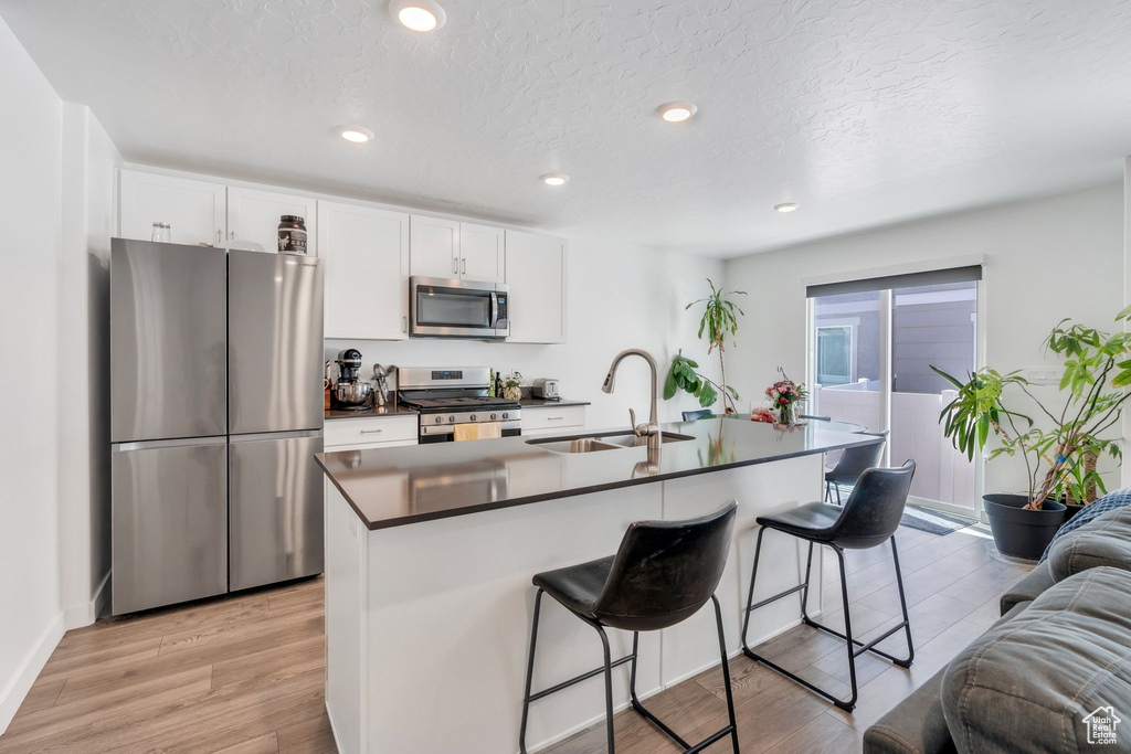 Kitchen with appliances with stainless steel finishes, a sink, dark countertops, a kitchen breakfast bar, and white cabinetry