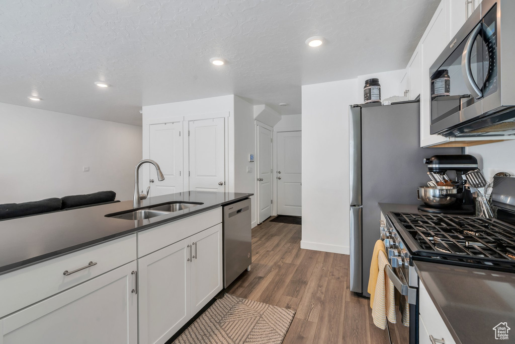 Kitchen with stainless steel appliances, a sink, dark countertops, white cabinets, and dark wood-style floors