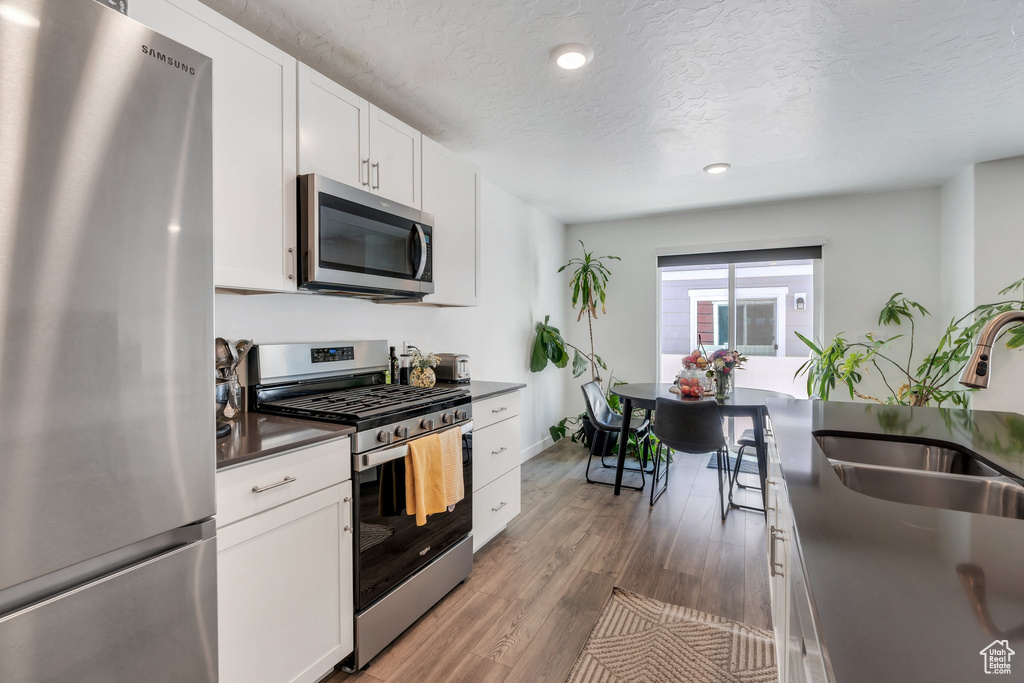 Kitchen with stainless steel appliances, a sink, dark countertops, a textured ceiling, and white cabinetry