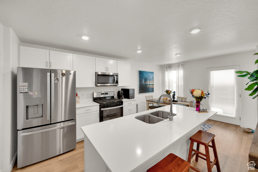 Kitchen with stainless steel appliances, a sink, white cabinetry, light wood-style flooring, and recessed lighting
