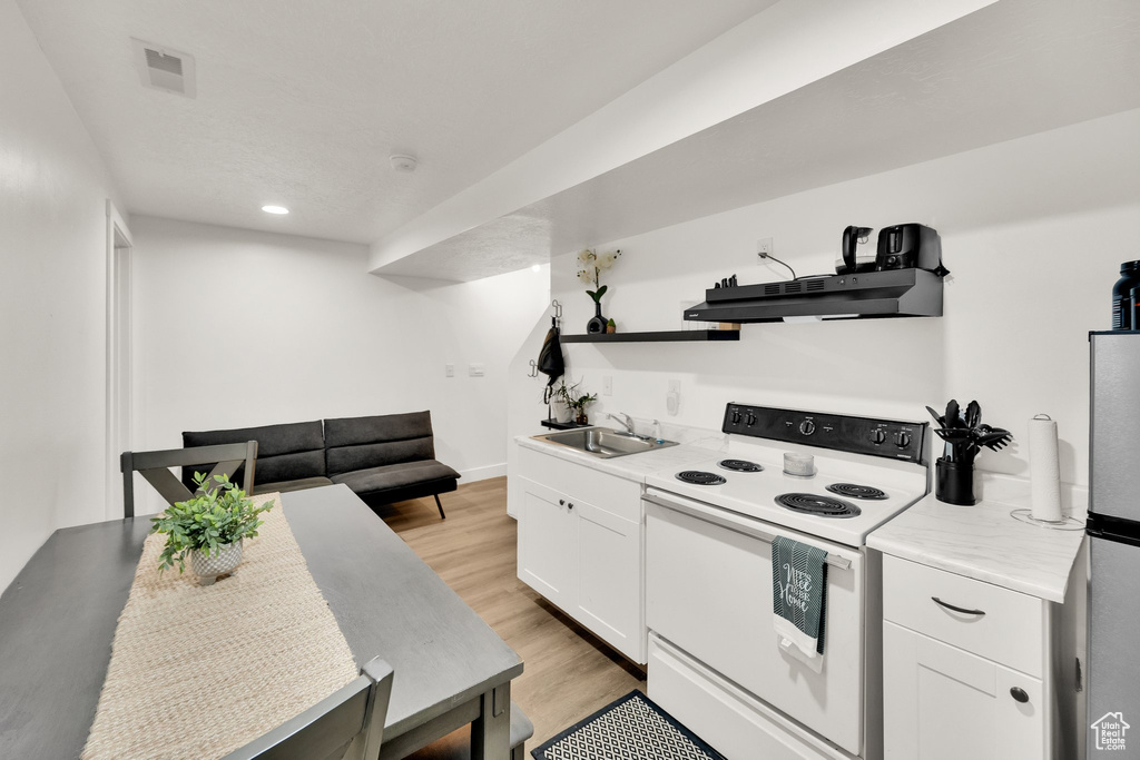 Kitchen featuring white range with electric stovetop, a sink, under cabinet range hood, freestanding refrigerator, and light countertops